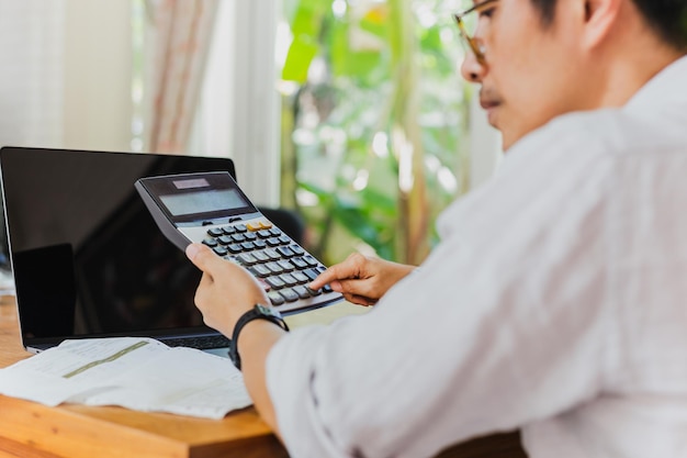 Zakenmanhand op rekenmachine om financieel rapport en laptopcomputer op tafel te berekenen