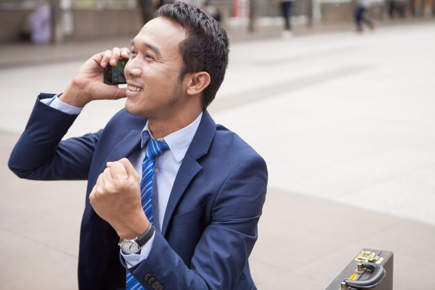 Zakenmanzitting op trede tijdens het roepen van de telefoon, met de bureaubouw achtergrond