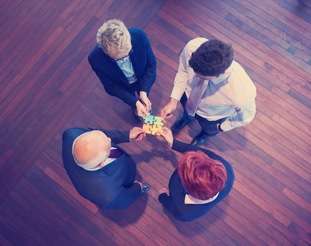 zakenmensen groep assembleren puzzel en vertegenwoordigen teamondersteuning en help concept, bovenaanzicht perspectief op modern, licht kantoorinterieur