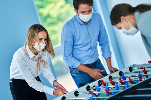 zakenmensen met beschermende maskers die tafeltennissen in gedeelde kantoorruimte