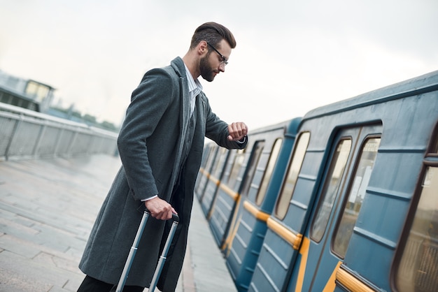 Zakenreis jonge zakenman die in de buurt van de spoorweg staat met bagage die de tijd controleert op het wachten op het horloge