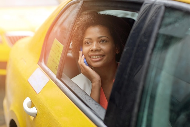 zakenreis, transport, reizen, gebaar en mensenconcept - jonge glimlachende Afro-Amerikaanse vrouw die smartphone in taxi op straat in de stad aanroept
