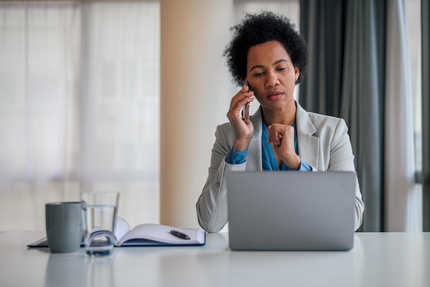 Zakenvrouw bespreken op slimme telefoon tijdens het werken op laptop op de werkplek