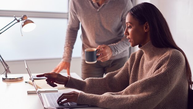 Zakenvrouw bezig met laptop aan bureau samen te werken met mannelijke collega koffie drinken