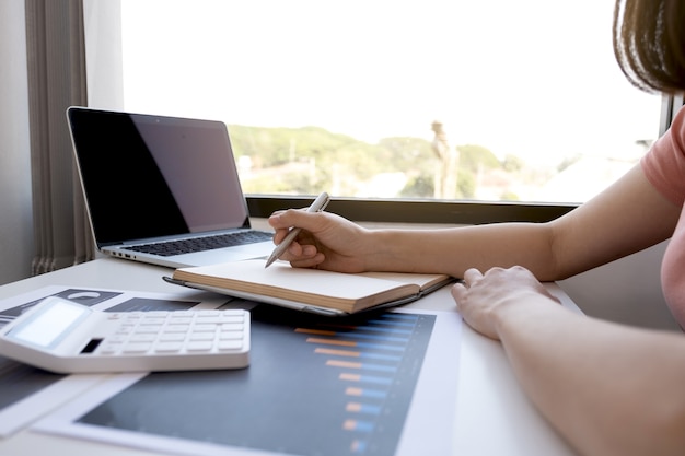 Zakenvrouw boekhouder hand nota analyse van de grafiek met rekenmachine en laptop op het kantoor aan huis