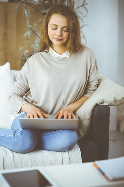 Foto zakenvrouw die aan een laptop werkt die binnen zit tijdens de quarantaine van covid-19 in een gezellige woonkamer. blijf thuis concept tijdens de pandemie van het coronavirus