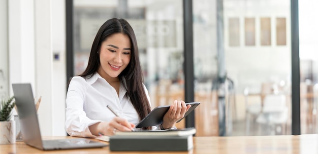 Zakenvrouw die een digitale tablet gebruikt terwijl ze op kantoor aan een laptop werkt Succesvolle vrouwelijke ondernemer