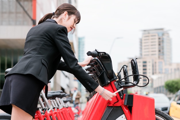 Zakenvrouw die een gedeelde elektrische fiets huurt op straat in de stad op weg naar haar werk
