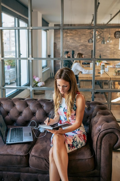 Zakenvrouw die met laptop werkt en aantekeningen maakt terwijl ze op de bank zit