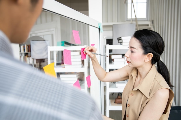 Zakenvrouw die op kantoor vergadert met gebruik van post-it-notities op een duidelijk bord om ideeën te delen die in de vergaderruimte werken.