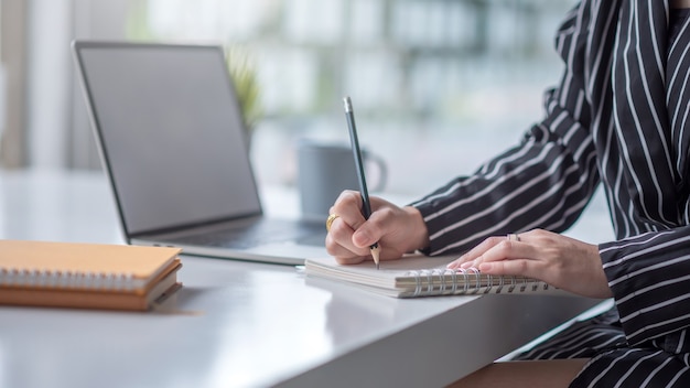 Zakenvrouw die op laptop werkt en nota neemt terwijl zittend aan de tafel op kantoor