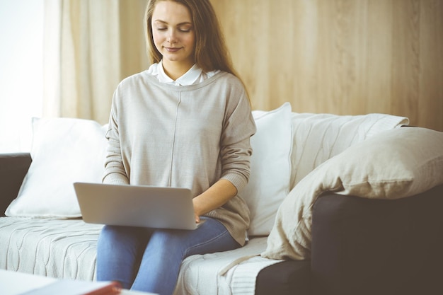 Zakenvrouw die op laptopcomputer werkt die binnenshuis zit tijdens Covid-19 quarantaine in een gezellige woonkamer. Blijf thuis concept tijdens de pandemie van het Coronavirus.