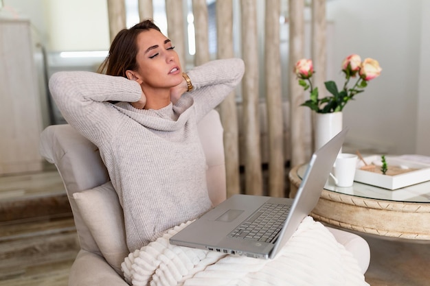 Zakenvrouw die pijn in de nek voelt nadat ze met een laptop aan tafel zit. Vermoeide vrouw die lijdt aan het kantoorsyndroom vanwege lange uren computerwerk. Mooi meisje dat haar gespannen nekspieren masseert