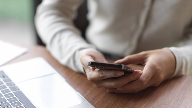 Zakenvrouw die smartphone met laptop op het houten bureau gebruikt