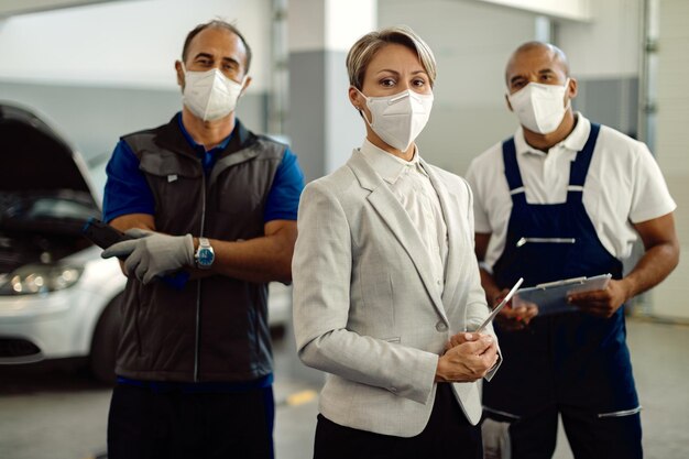 Zakenvrouw en automonteurs met beschermende gezichtsmaskers bij autoservicewinkel