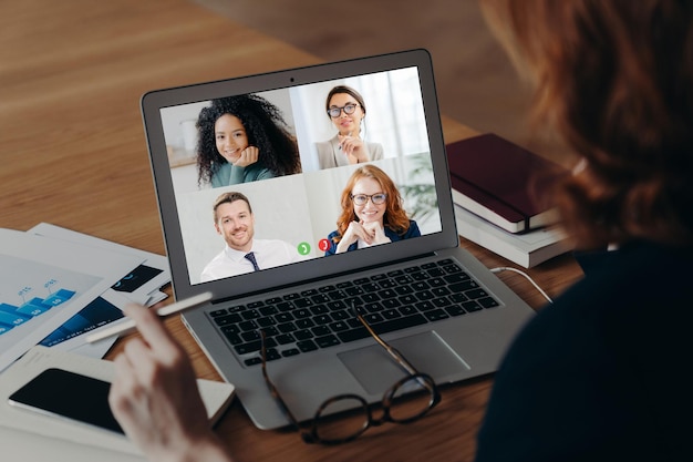 Zakenvrouw gebruikt laptop applicatie voor communicatie met meerdere mensen heeft virtuele conferentie werkt freelance vanuit huis zit op desktop omringd met papieren documenten Online onderhandelingen