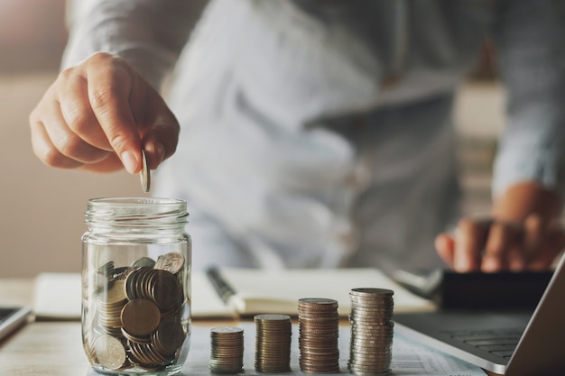 zakenvrouw geld besparen met de hand putting munten in kruik glas