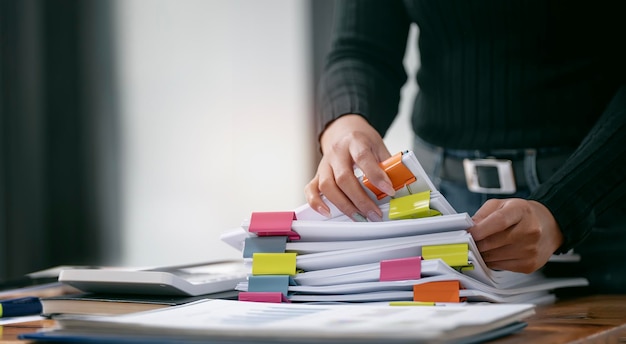 Zakenvrouw handen werken in stapels papieren bestanden voor het zoeken en controleren van onvoltooide documenten bereikt op mappenpapier