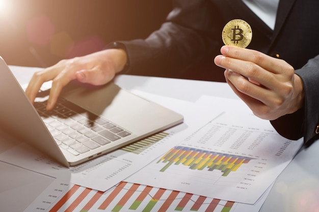 Zakenvrouw houdt Bitcoin cryptocurrency werkelijke munt in de hand om gedecentraliseerde financiële mockup kopie ruimte te presenteren op zwarte achtergrond met computer laptop grafiek op tafel