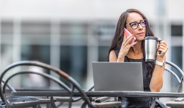 Foto zakenvrouw houdt koffiemok en luistert naar een persoon op een telefoon met een geopende computer voor haar