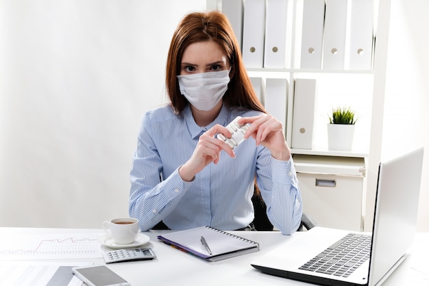 zakenvrouw in een masker op de werkplek heeft een tablet in haar handen