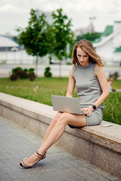 Zakenvrouw in elegante jurk met laptop op straat