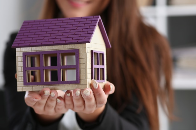 Zakenvrouw in het kantoor heeft een miniatuur speelgoed huis in haar hand