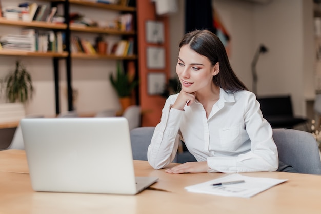 Zakenvrouw in het kantoor met laptop maakt online verbinding met klanten