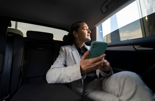 Zakenvrouw in mobiele personenauto op achterbank met smartphone