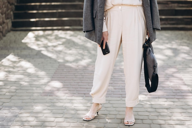 Zakenvrouw in pak en grijze jas met zakelijke accessoires tas bril telefoon