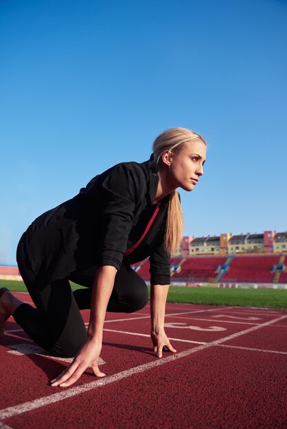 zakenvrouw in startpositie klaar om te rennen en sprinten op atletiekbaan