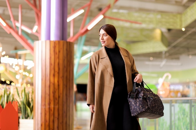 Foto zakenvrouw loopt zelfverzekerd stijlvol gekleed met jas en handtas glimlachend en opzij kijkend