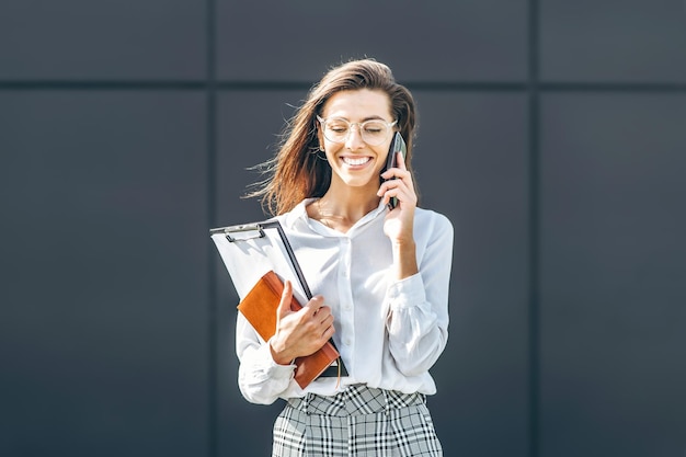 Zakenvrouw lopend en pratend op de mobiele telefoon buiten in de buurt van modern zakencentrum met notebook