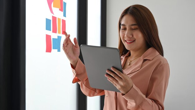 Zakenvrouw met behulp van digitale tablet en het lezen van plaknotities op glazen wand