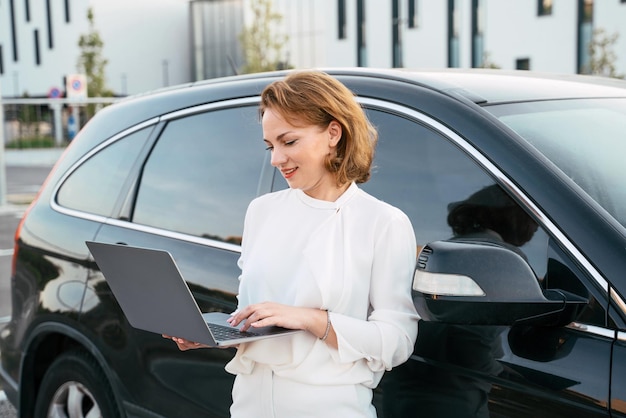 Zakenvrouw met behulp van laptopcomputer die online werkt in de buurt van auto. Succesvol bedrijf