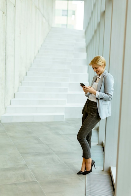 Zakenvrouw met behulp van mobiele telefoon op moderne kantoor hal