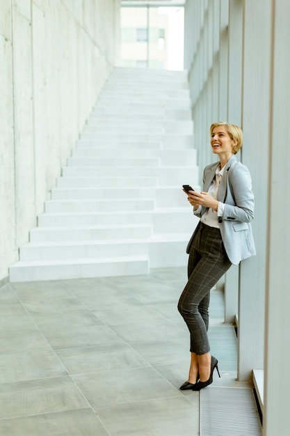 Zakenvrouw met behulp van mobiele telefoon op moderne kantoor hal