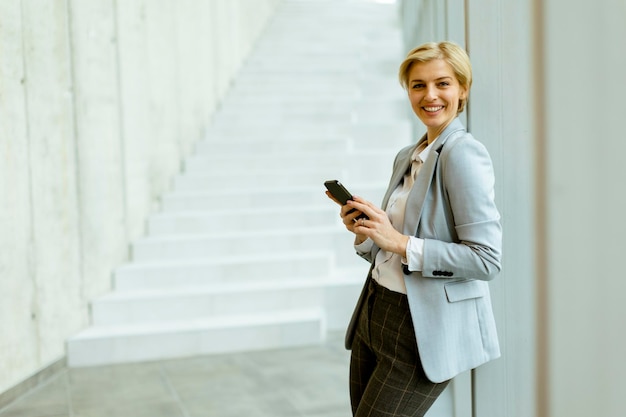 Zakenvrouw met behulp van mobiele telefoon op moderne kantoor hal