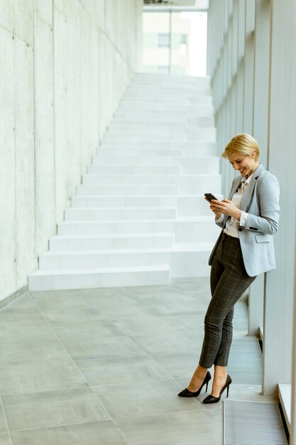 Zakenvrouw met behulp van mobiele telefoon op moderne kantoor hal