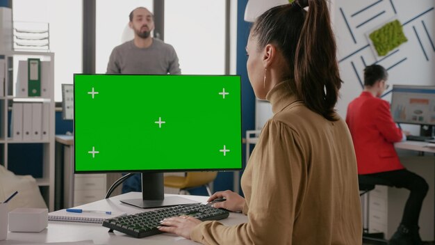 Zakenvrouw met behulp van monitor met groen scherm in opstarten kantoor, kijken naar chroma key en mock up geïsoleerde achtergrond op computer. Weergeven met lege sjabloon voor kopieerruimte