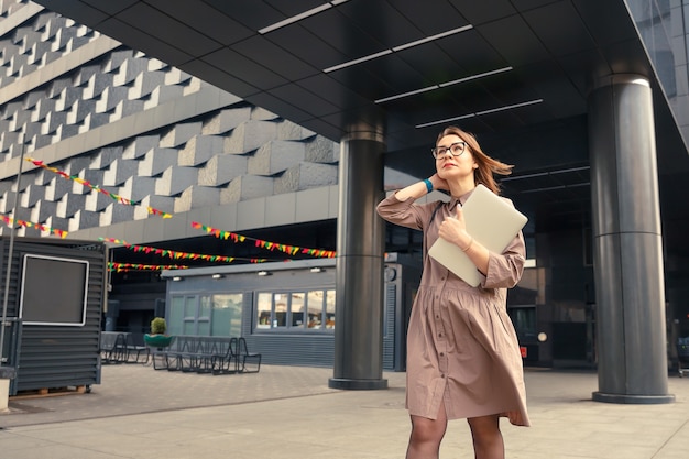 Zakenvrouw met computer op de achtergrond van een modern zakelijk gebouw.