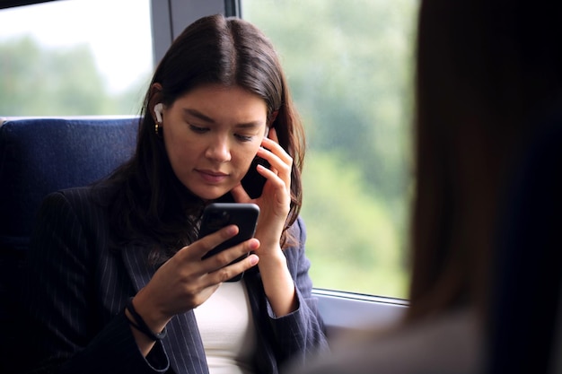 Zakenvrouw met draadloze oordopjes woon-werkverkeer in de trein kijken naar mobiele telefoon