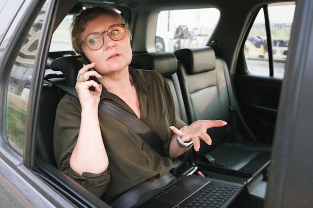 Zakenvrouw met een bril praat aan de telefoon terwijl ze op de achterbank van een auto zit