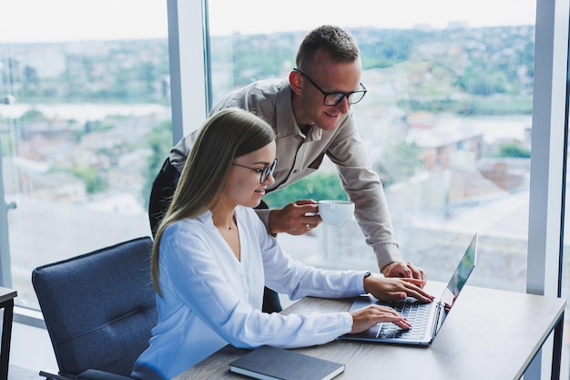 Zakenvrouw met een laptop voor een mannelijke collega die naar een open notitieboekje kijkt zakelijke samenwerking en teamwork europese millennials aan de tafel op kantoor moderne succesvolle mensen