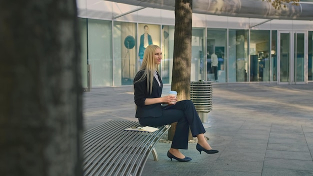 zakenvrouw met een wegwerpbeker die op een stoel in de stad zit
