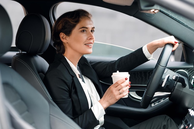 zakenvrouw met een wegwerpkoffiekop terwijl ze een auto rijdt