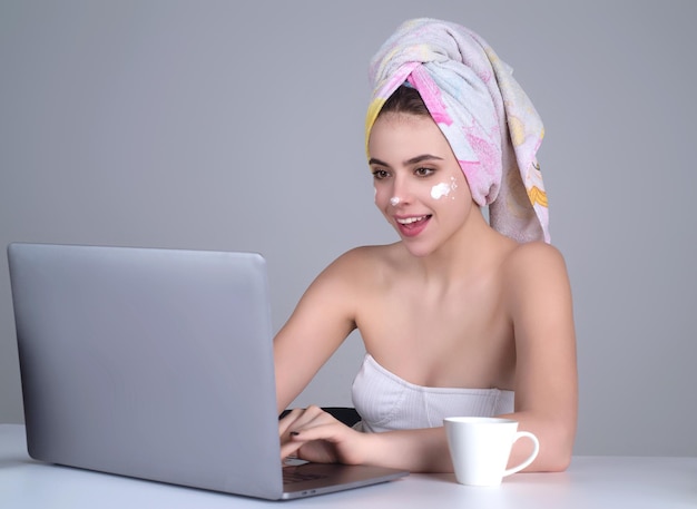 Zakenvrouw met handdoek op hoofd gezichtscrème op gezicht houd kopje koffie bezig met laptop ochtend