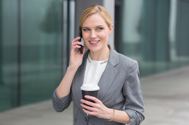 Zakenvrouw met koffie in haar hand terwijl ze aan het praten is met haar smartphone