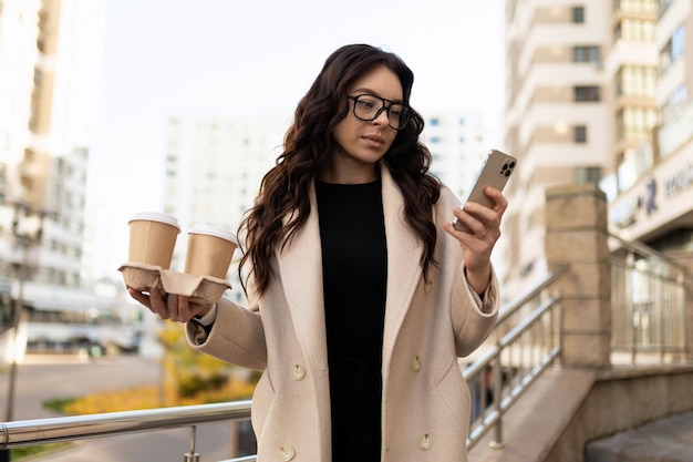 Zakenvrouw met kopjes koffie kijken naar de telefoon