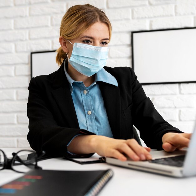 Zakenvrouw met medisch masker op kantoor met laptop werken